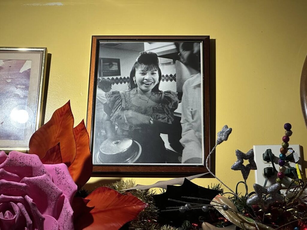 Framed black-and-white photograph of a smiling young server holding a tray inside Mi Tierra Café decades ago