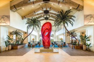 Margaritaville Resort Orlando lobby with a large glossy red flip-flop sculpture framed by palm trees and vaulted ceilings.