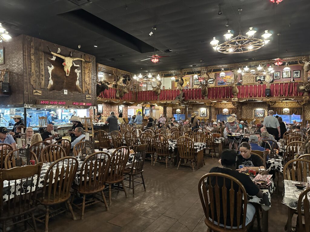 Interior of The Big Texan Steak Ranch in Amarillo, Texas, with Western décor, cow-print tablecloths, and diners seated throughout the restaurant.