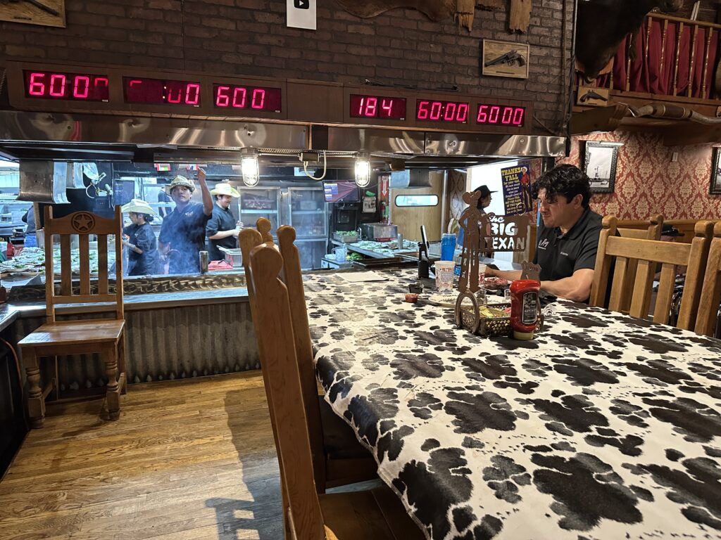 Dining table near the open kitchen at The Big Texan Steak Ranch with red digital timers for the 72-ounce steak challenge above the grill.