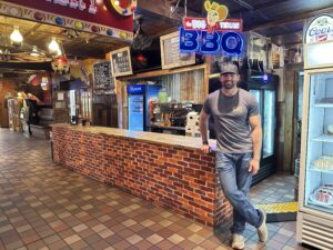 Patrick, third-generation family member of The Big Texan Steak Ranch, standing inside the Amarillo restaurant near a neon Big Texan BBQ sign.