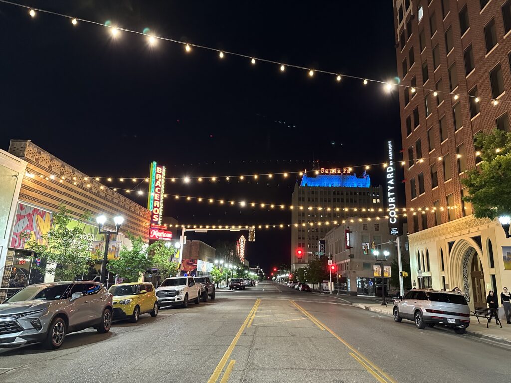 Downtown Amarillo street at night with string lights, neon signs, parked cars, and the Courtyard Marriott building on the right.
