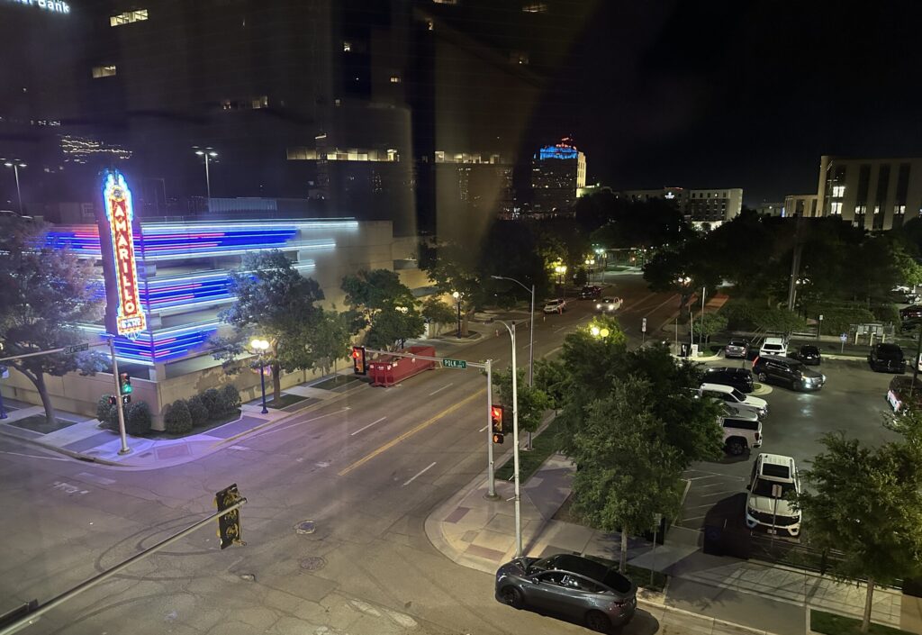 Night view from a hotel room in downtown Amarillo, Texas, showing city streets, parked cars, and the illuminated Amarillo National Bank sign.