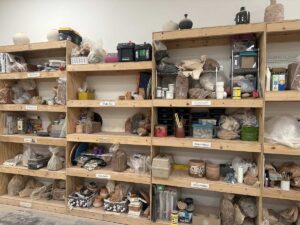 Shelving inside an artist studio at Arts in the Sunset filled with clay, pottery tools, supplies, and ceramic works in progress.
