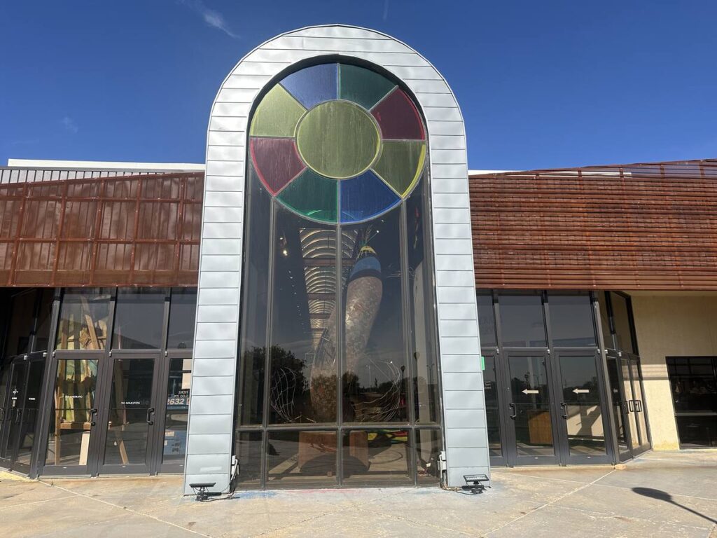 Exterior entrance of Arts in the Sunset in Amarillo, Texas, with a tall arched window and colourful stained-glass detail.