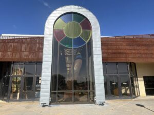 Exterior entrance of Arts in the Sunset in Amarillo, Texas, with a tall arched window and colourful stained-glass detail.