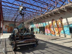 Outdoor courtyard at Arts in the Sunset with colourful tiger murals, exposed steel beams, and a large sculptural installation.