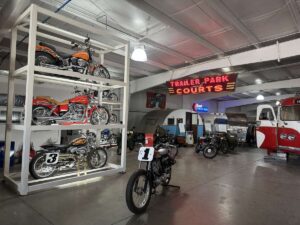 Interior of the Jack Sisemore Traveland RV Museum in Amarillo, Texas, showing vintage motorcycles, trailers, a red-and-white bus, and a neon “Trailer Park and Courts” sign.