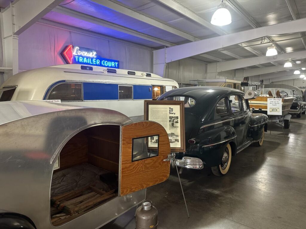 Vintage trailers, a black classic car, and a neon Locust Trailer Court sign displayed inside the Jack Sisemore Traveland RV Museum in Amarillo.