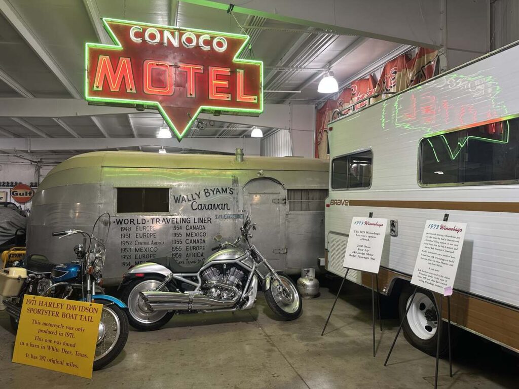 Vintage RVs, motorcycles, a Conoco Motel neon sign, and travel memorabilia displayed inside the Jack Sisemore Traveland RV Museum.