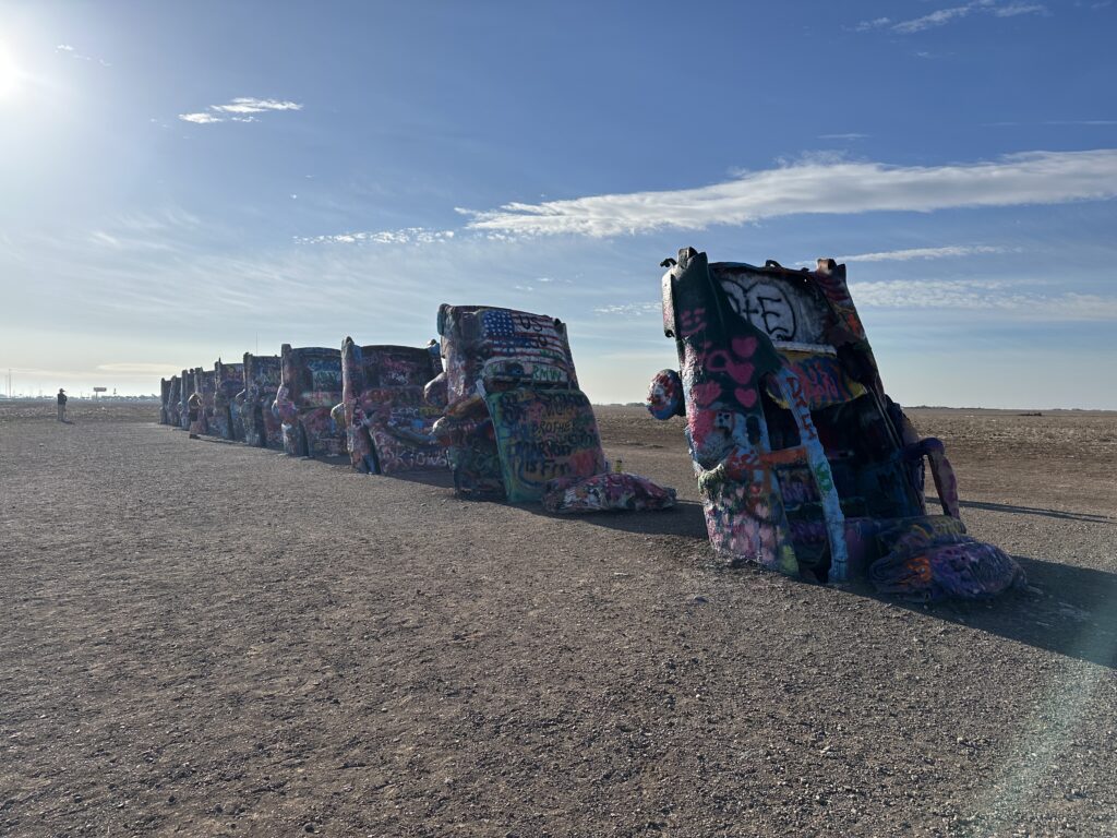 Cadillac Ranch in Amarillo, Texas, with spray-painted Cadillacs buried nose-first in an open field beneath a bright blue sky.