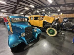 Blue wood-panelled classic car and yellow vintage car displayed side by side inside Bill’s Backyard Classics.