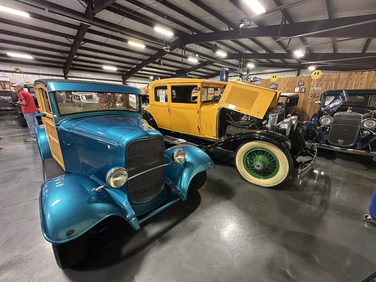 Blue wood-panelled classic car and yellow vintage car displayed side by side inside Bill’s Backyard Classics.