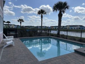 A private cottage pool overlooking a pond, palm trees, and pastel resort homes under a bright sky.