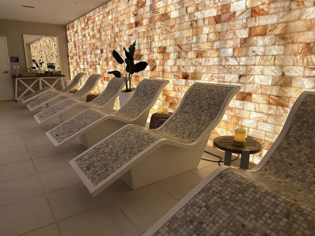 Curved spa loungers arranged beside a glowing salt wall with candles and soft lighting.