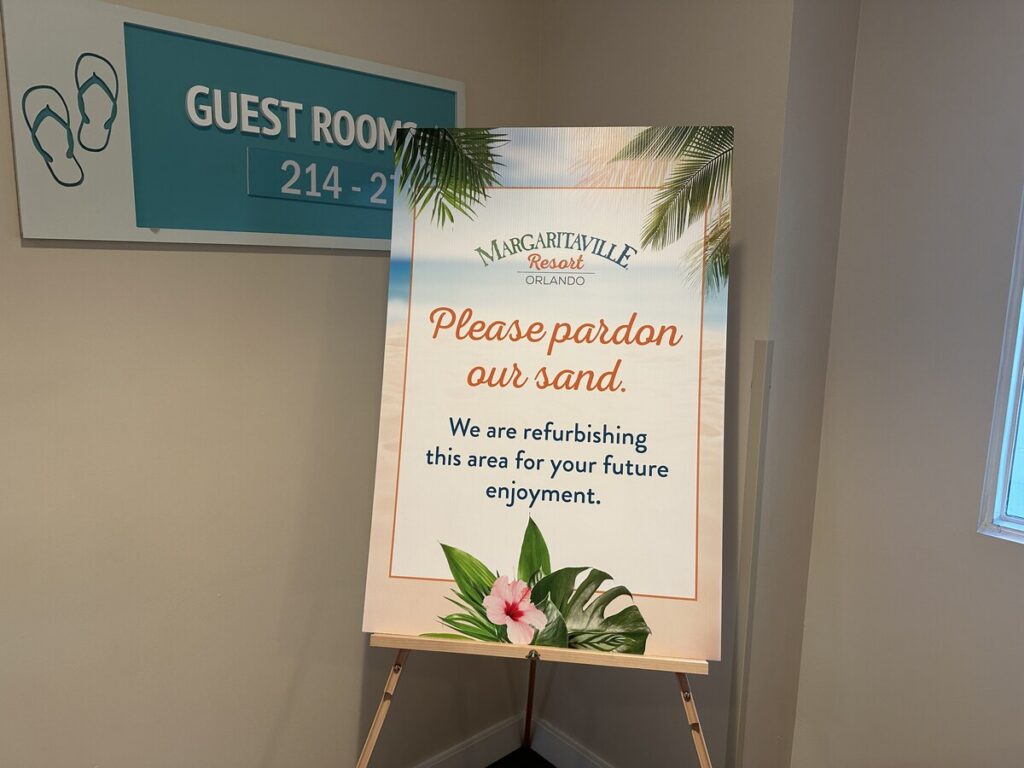 Margaritaville Resort sign reading “Please pardon our sand” beside a guest room directional sign.