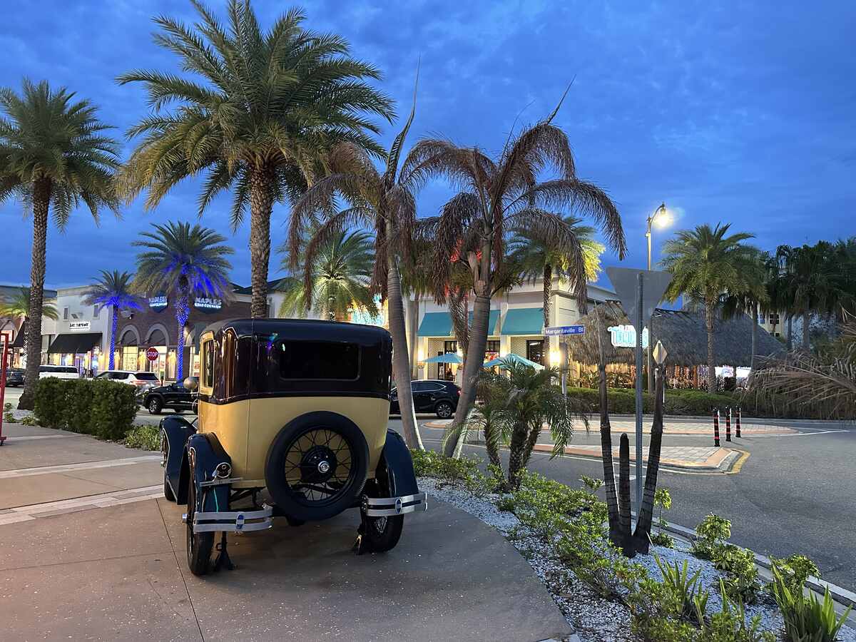 Vintage car parked near palm trees and illuminated shops at Margaritaville Resort Orlando in the evening.