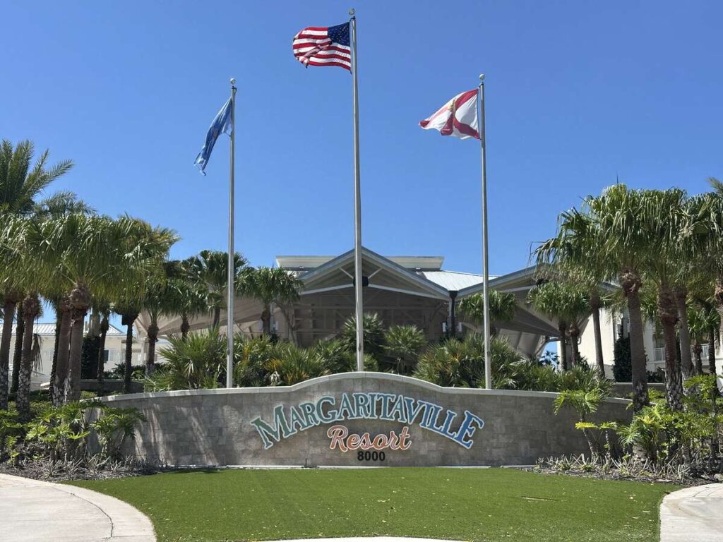 Margaritaville Resort Orlando entrance sign with palm trees, flags, and a bright blue sky.
