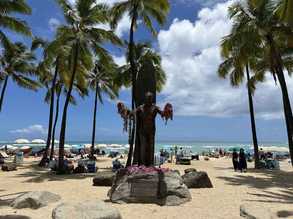 Duke Kahanamoku Statue on Waikīkī Beach with leis and ocean behind it.