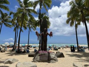 Duke Kahanamoku Statue on Waikīkī Beach with leis and ocean behind it.