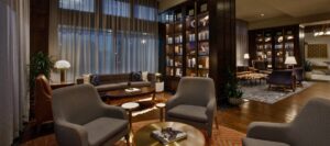 Lounge area inside The Barfield hotel in downtown Amarillo, Texas, with upholstered chairs, wood floors, tall windows, and illuminated bookshelves.