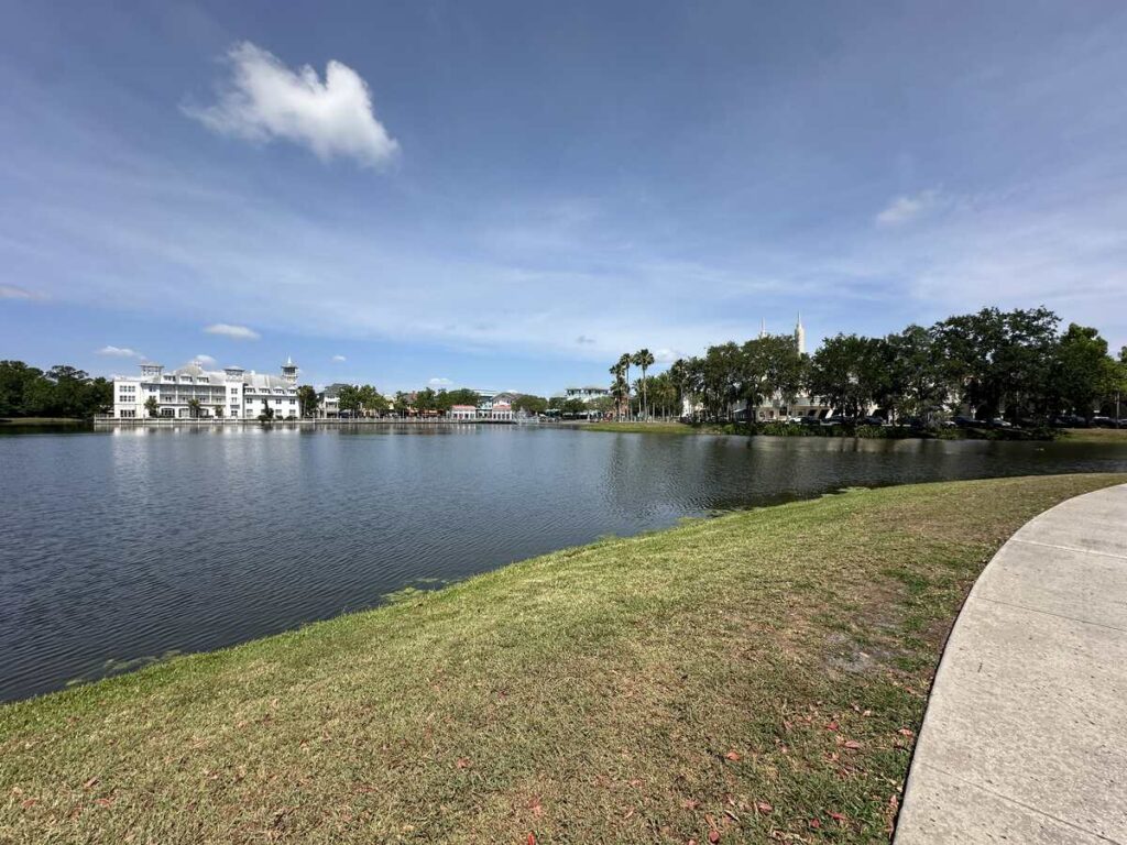 Wide lake view in Celebration, Florida, with a curved path, grassy shoreline, and white buildings across the water.