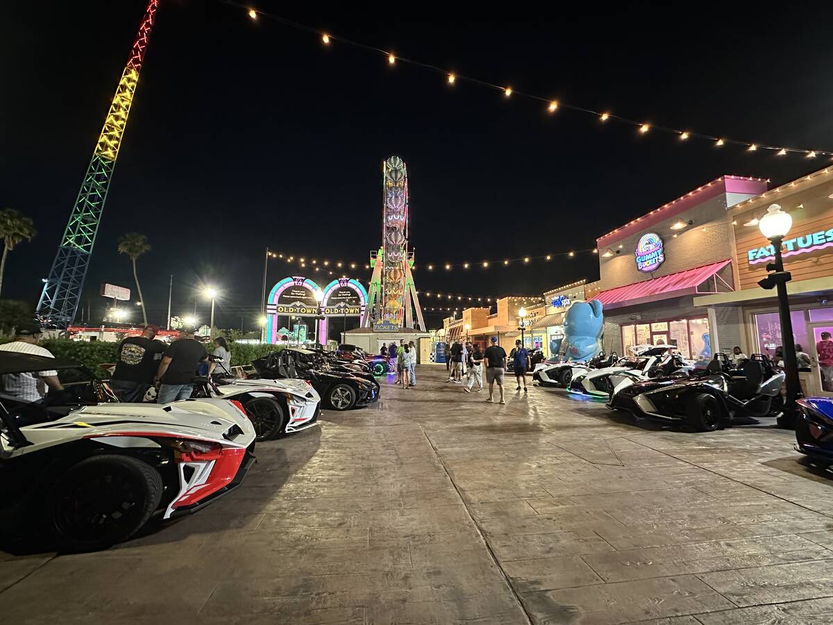 Evening scene at Old Town Kissimmee with parked three-wheeled vehicles, string lights, storefronts, and amusement rides.