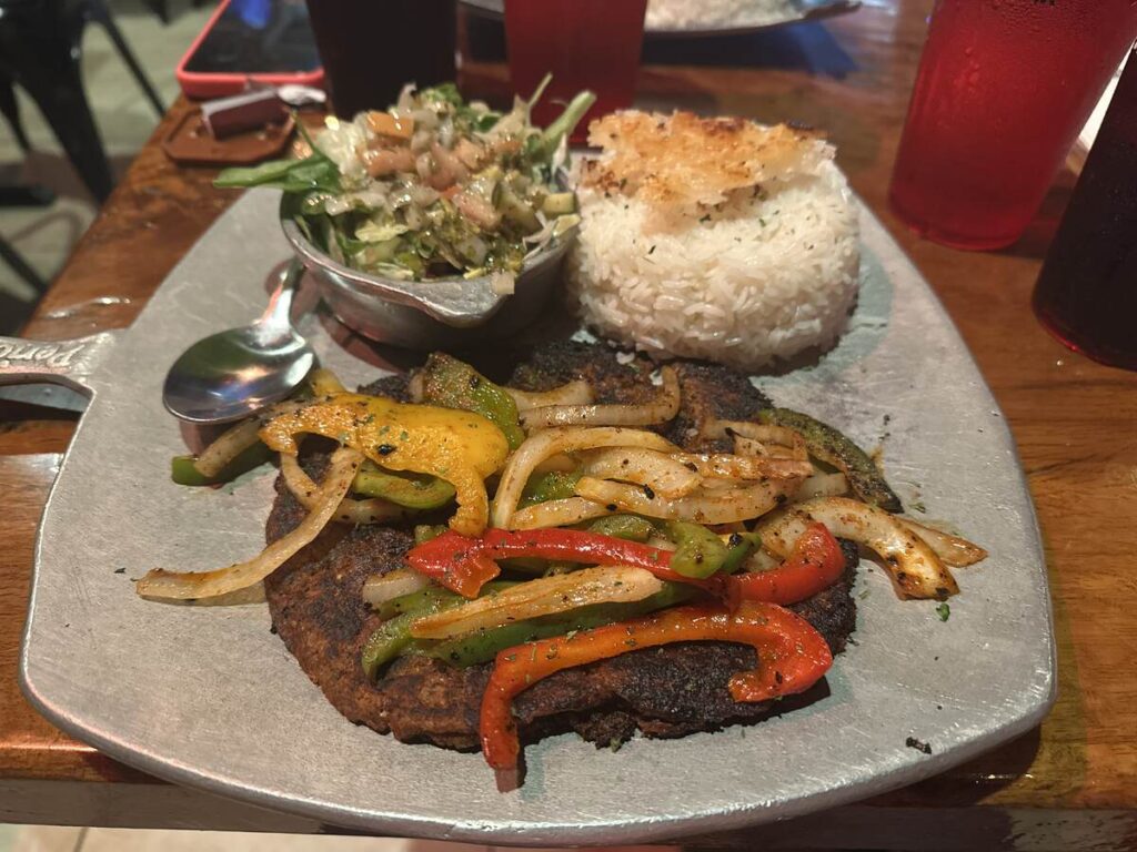 Latin dinner plate with grilled meat, peppers, onions, rice, salad, and a crispy topping, likely at El Cilantrillo in Kissimmee.