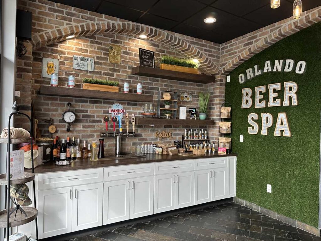 Reception area at Orlando Beer Spa with taps, shelves, brick walls, and a green wall reading “Orlando Beer Spa.”
