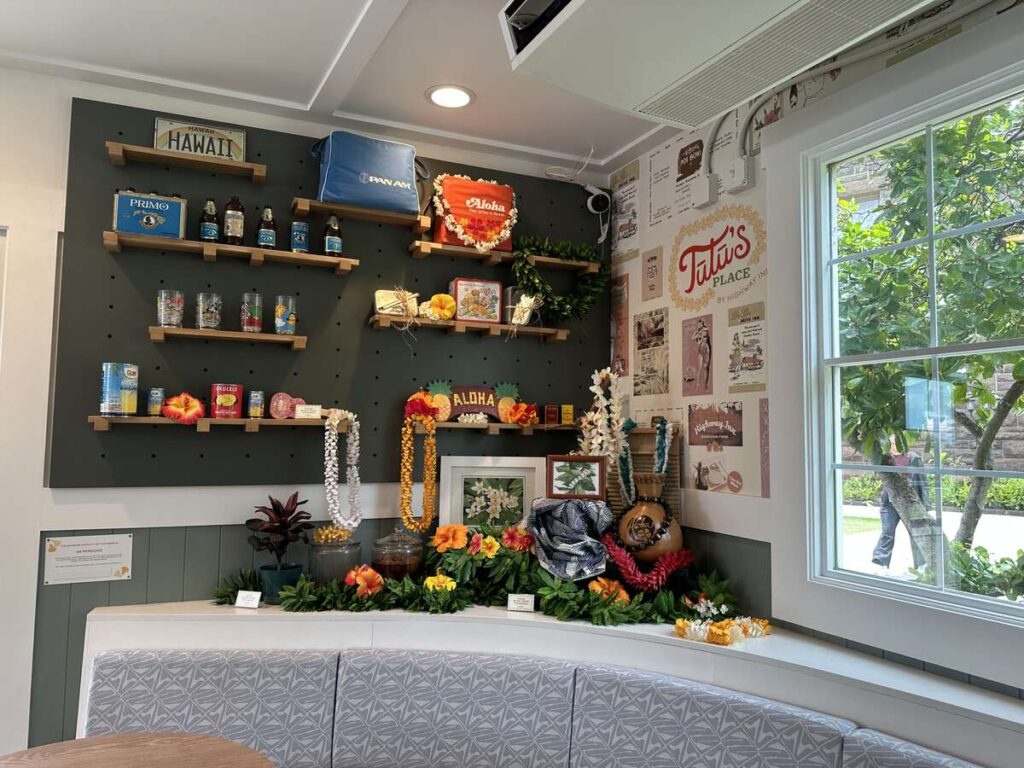 A colourful history display inside Tūtū’s Place by Highway Inn, featuring Hawaiian keepsakes, leis, vintage packaging, and family restaurant memorabilia.