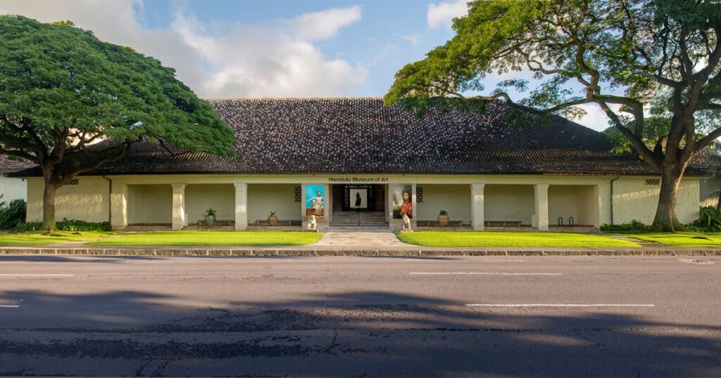 Exterior view of the Honolulu Museum of Art, framed by trees and open lawn.