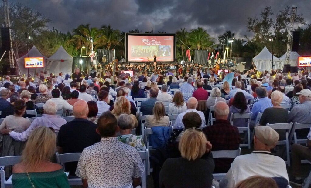 Outdoor audience seated at night for an Opera Naples festival performance with a large screen and orchestra stage.