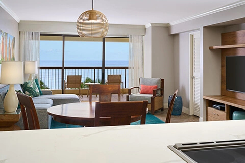 Ocean-view suite living area with dining table, kitchenette counter, balcony, and seating at Aston Waikīkī Beach Tower.