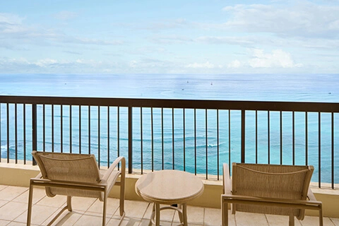 Balcony with two chairs and a small table overlooking the blue ocean at Aston Waikīkī Beach Tower.