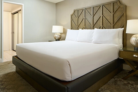 Neutral bedroom with king bed, white linens, lamps, and textured headboard at Aston Waikīkī Beach Tower.