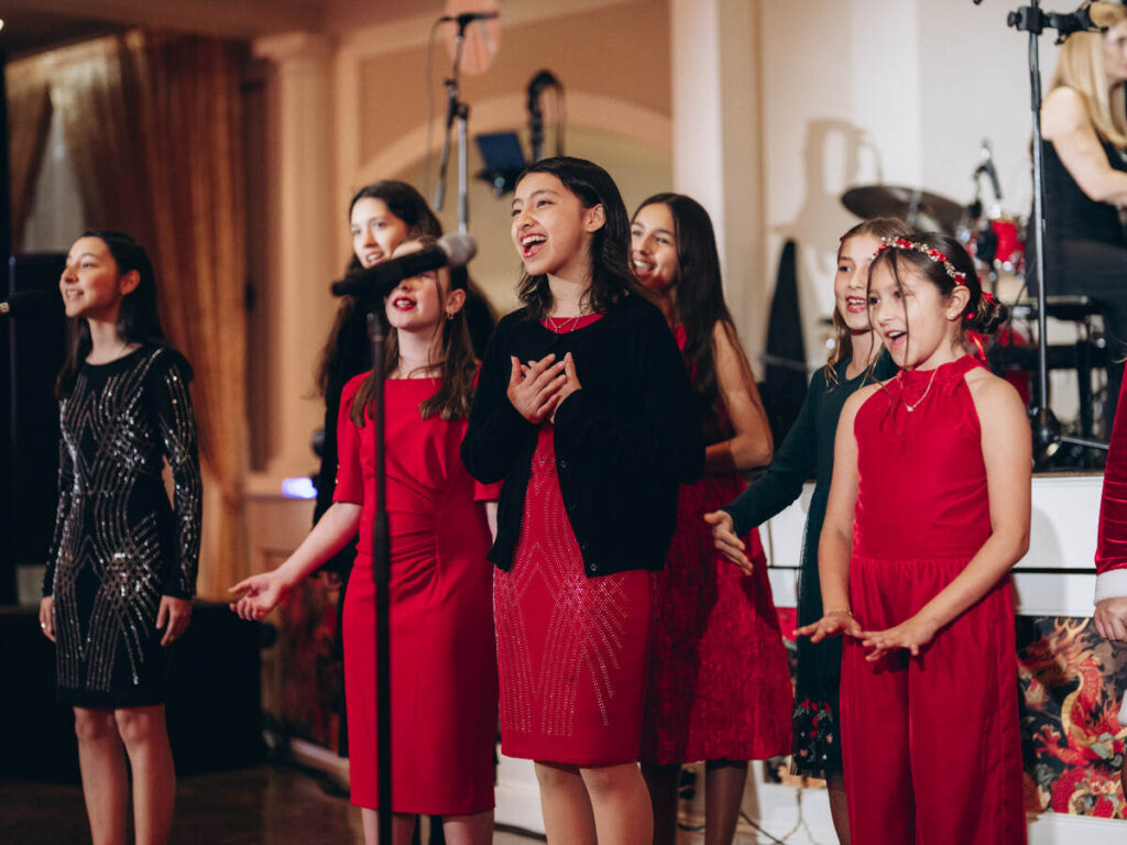 Young singers in red and black performing together on stage with microphones nearby.