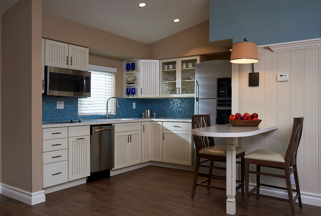 Condo-style kitchen inside a suite at Edgewater Beach Hotel in Naples, with white cabinets, blue tile backsplash, stainless steel appliances, and a breakfast bar.