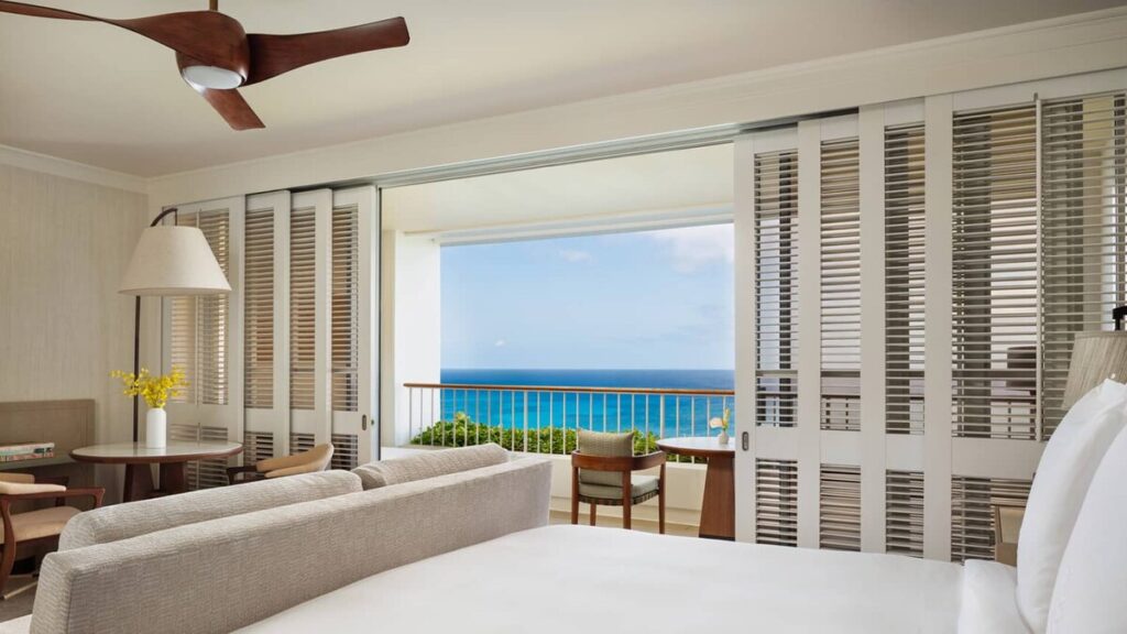 Guest room at Four Seasons Resort Oahu at Ko Olina with ocean-view balcony, bed, sitting area, and louvered doors.