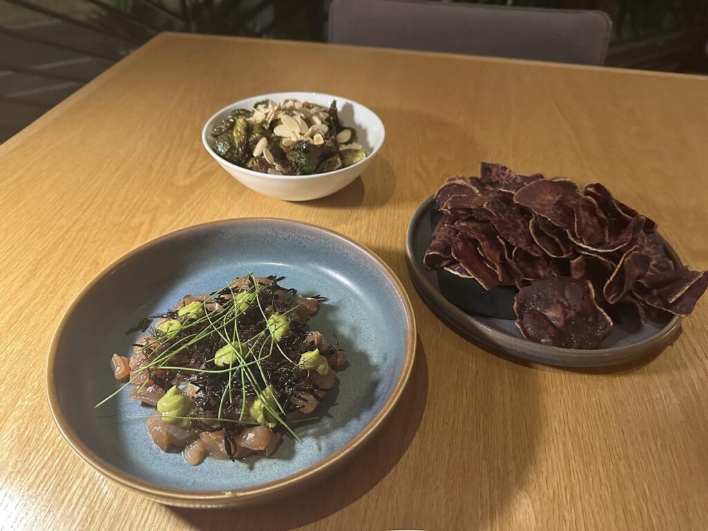 Smoked ahi poke, purple sweet potato chips, and Brussels sprouts served on a wooden table at Arden Waikīkī.