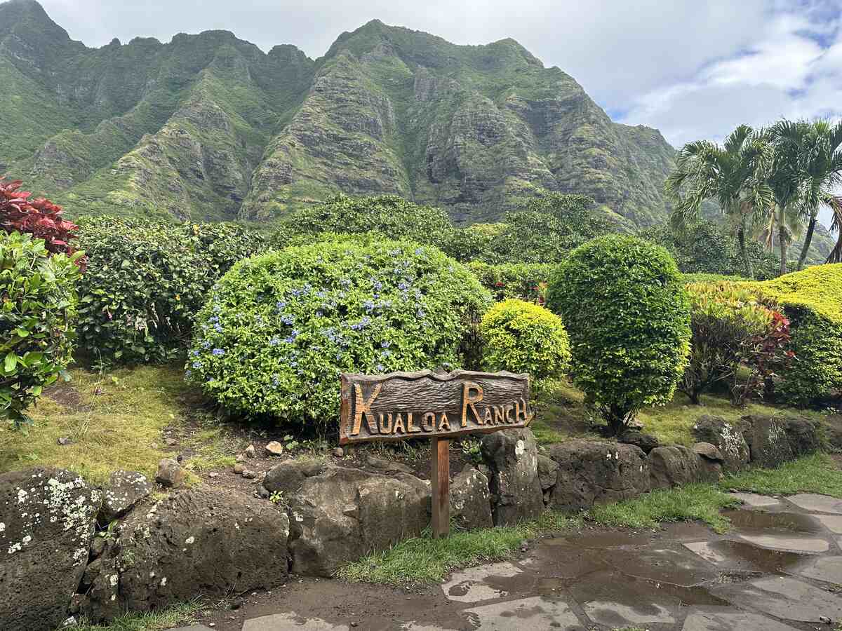 Kualoa Ranch sign with lush green mountains rising dramatically in the background.