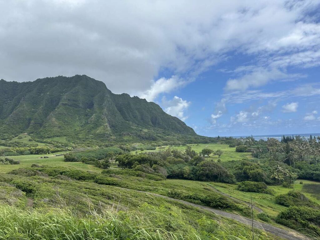 Green Kualoa valley landscape with mountains, fields, and ocean in the distance.
