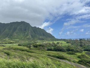 Green Kualoa valley landscape with mountains, fields, and ocean in the distance.