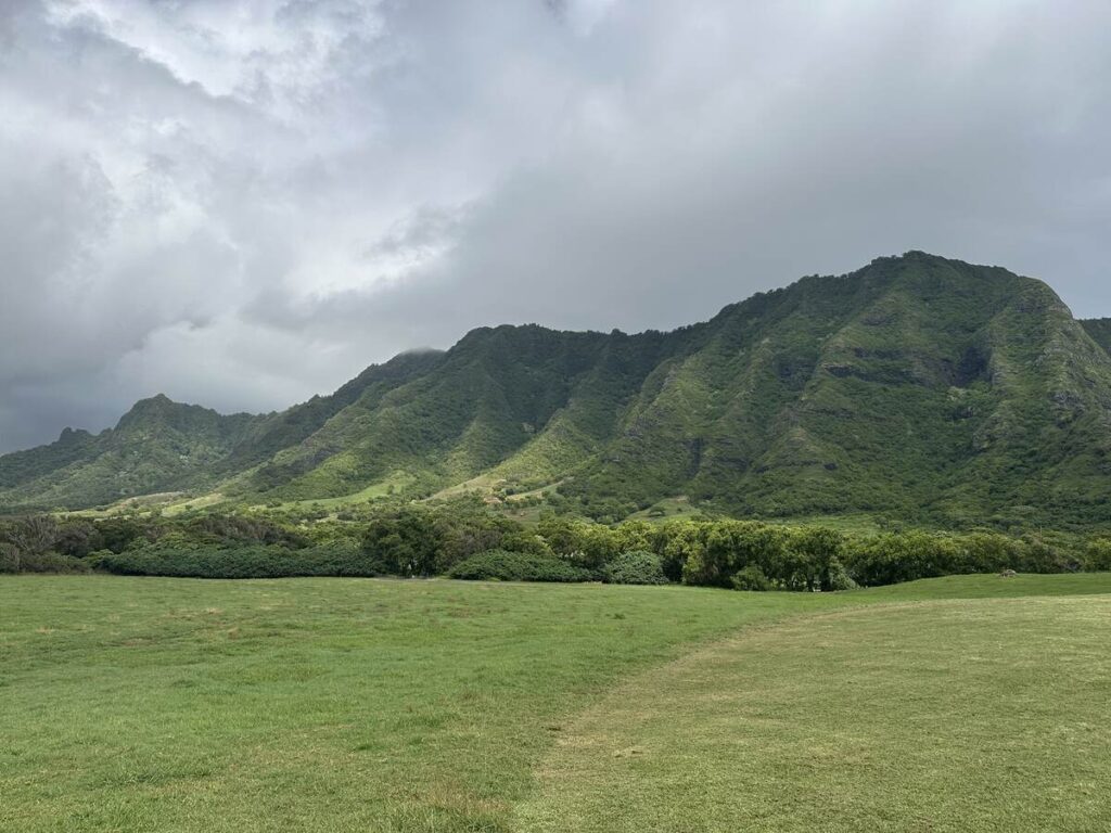 Open green valley at Kualoa Ranch with steep mountains under a cloudy sky.