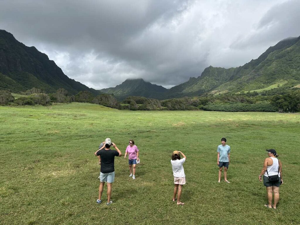 Visitors take photos in a wide green valley surrounded by mountains at Kualoa Ranch.