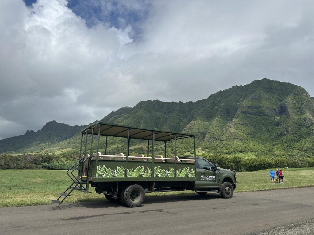 Open-air Kualoa Ranch tour vehicle parked in front of green mountains on Oʻahu.