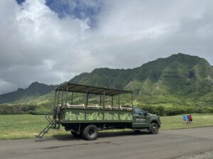 Open-air Kualoa Ranch tour vehicle parked in front of green mountains on Oʻahu.