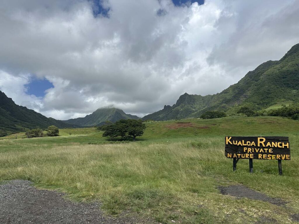 Kualoa Ranch Private Nature Reserve sign in a wide green valley surrounded by mountains.