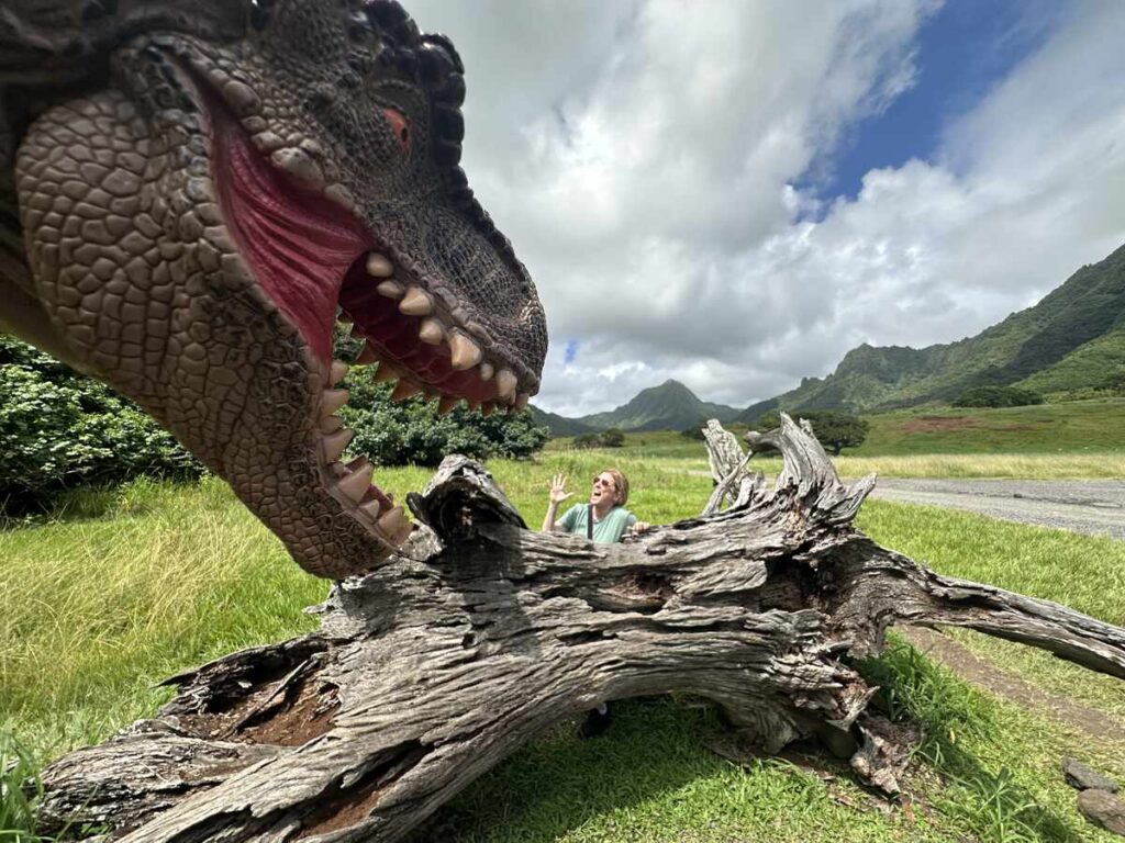 A dinosaur prop appears to lunge near a fallen log at a Jurassic Park photo stop.