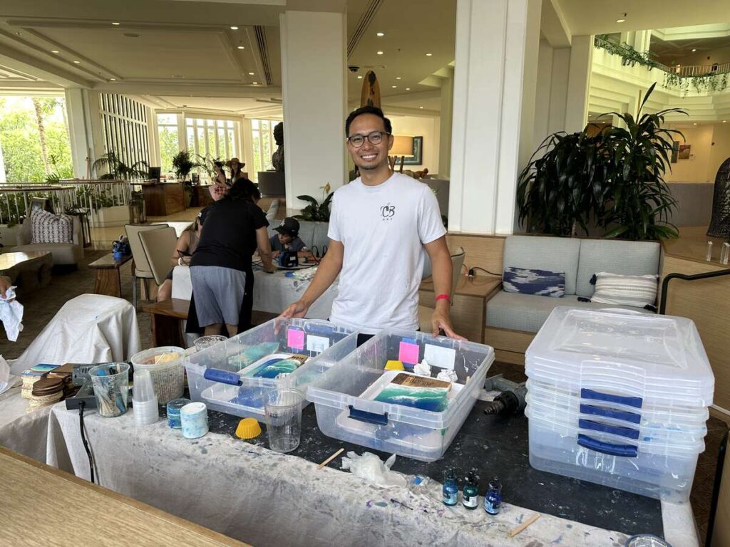 Local artist leading a resin painting workshop with miniature wooden surfboards and art supplies at Four Seasons Resort Oahu.