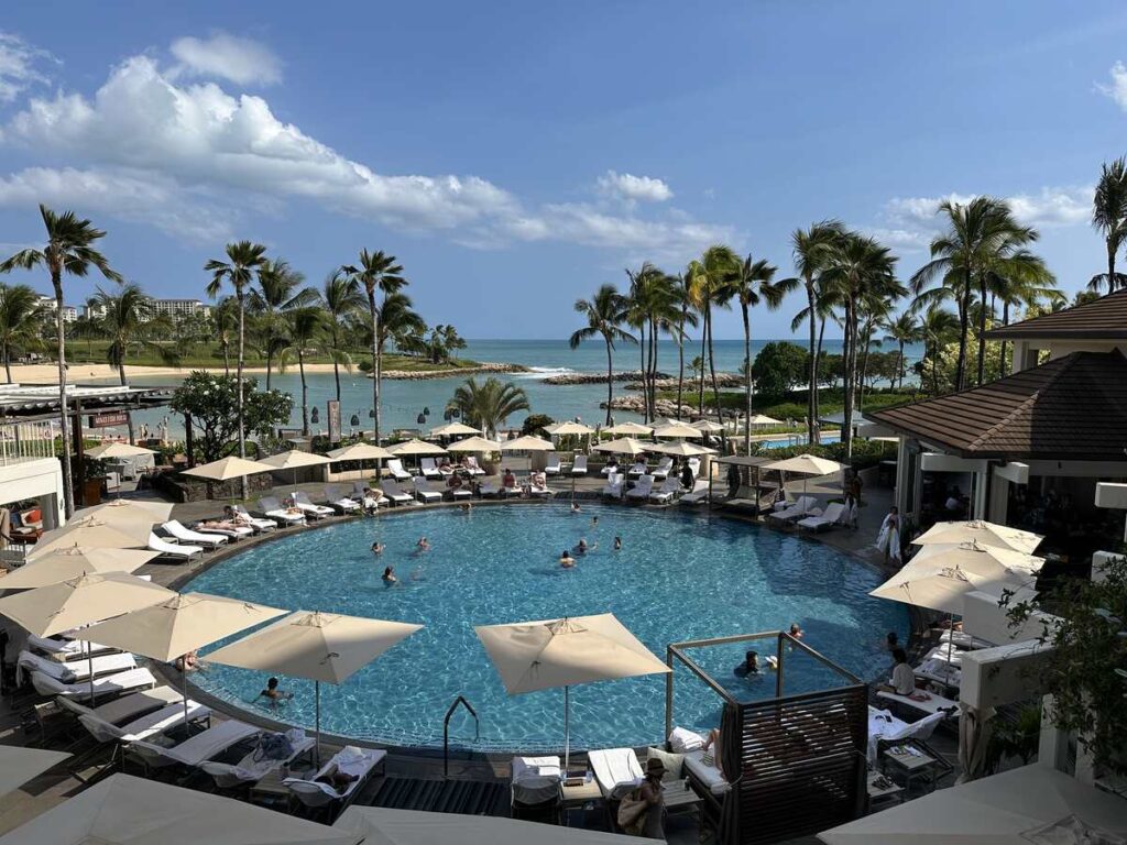 Resort pool with lounge chairs, umbrellas, palm trees, and ocean views at Ko Olina.